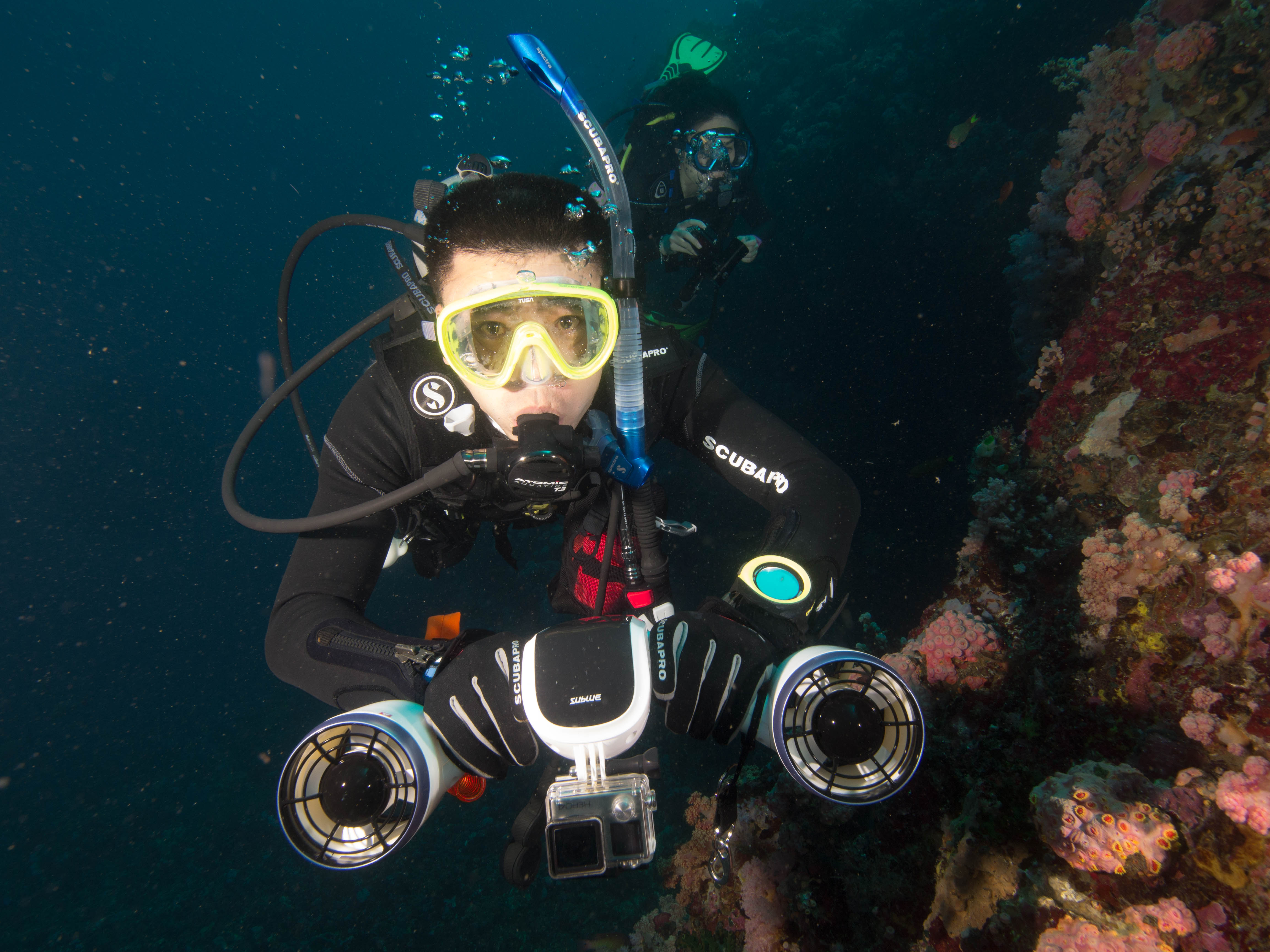 Diver using Sublue underwater scooter near colorful coral reef.