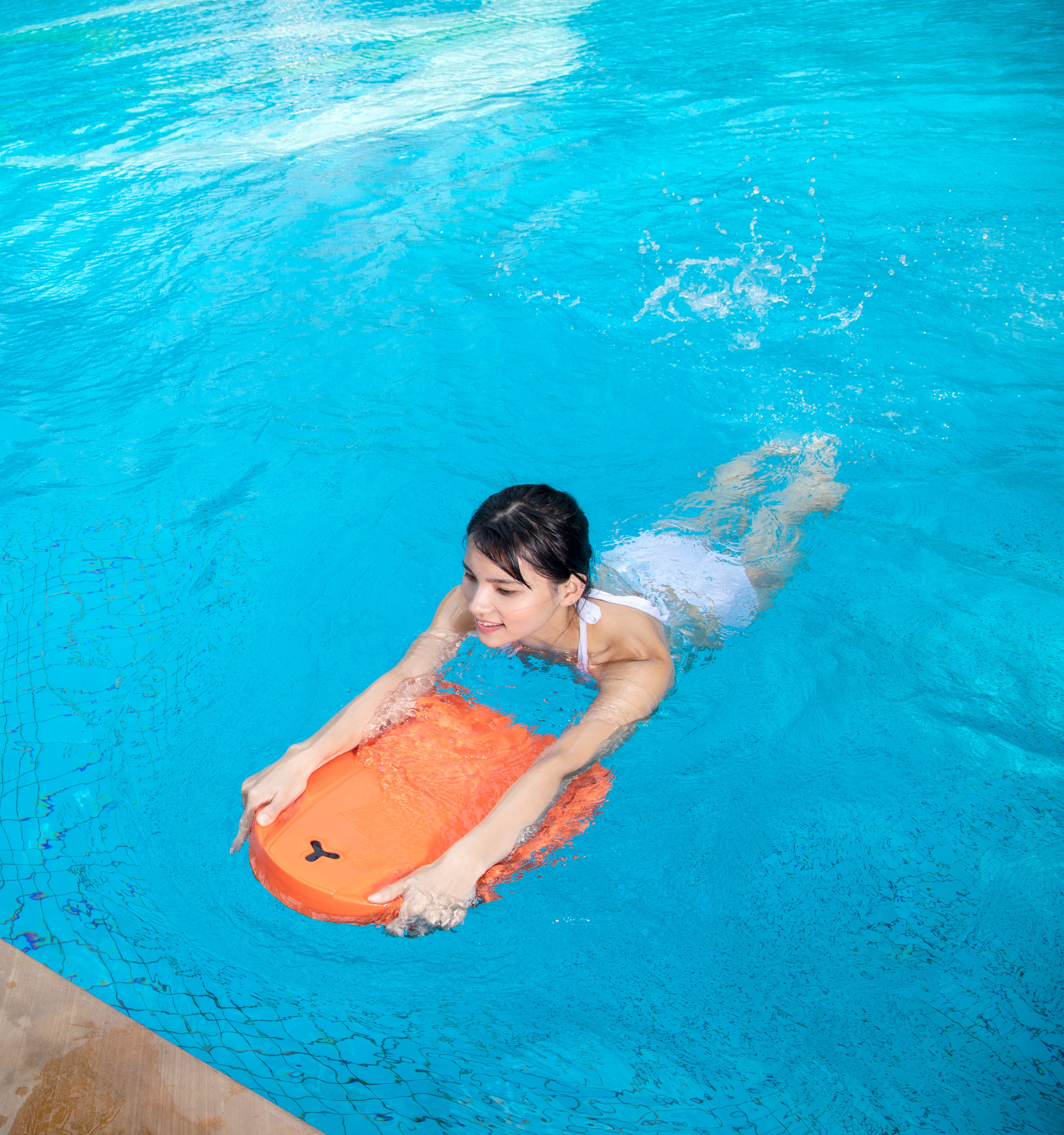 Woman swimming with orange SUBLUE Swii kickboard in blue pool.