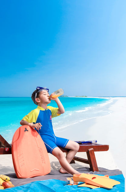 Child in swim gear enjoying a drink with SUBLUE kickboard on a sunny beach.