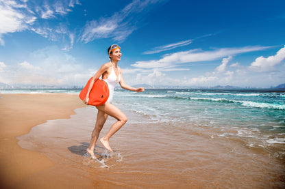 Woman in white swimsuit carrying orange SUBLUE Swii kickboard on the beach.