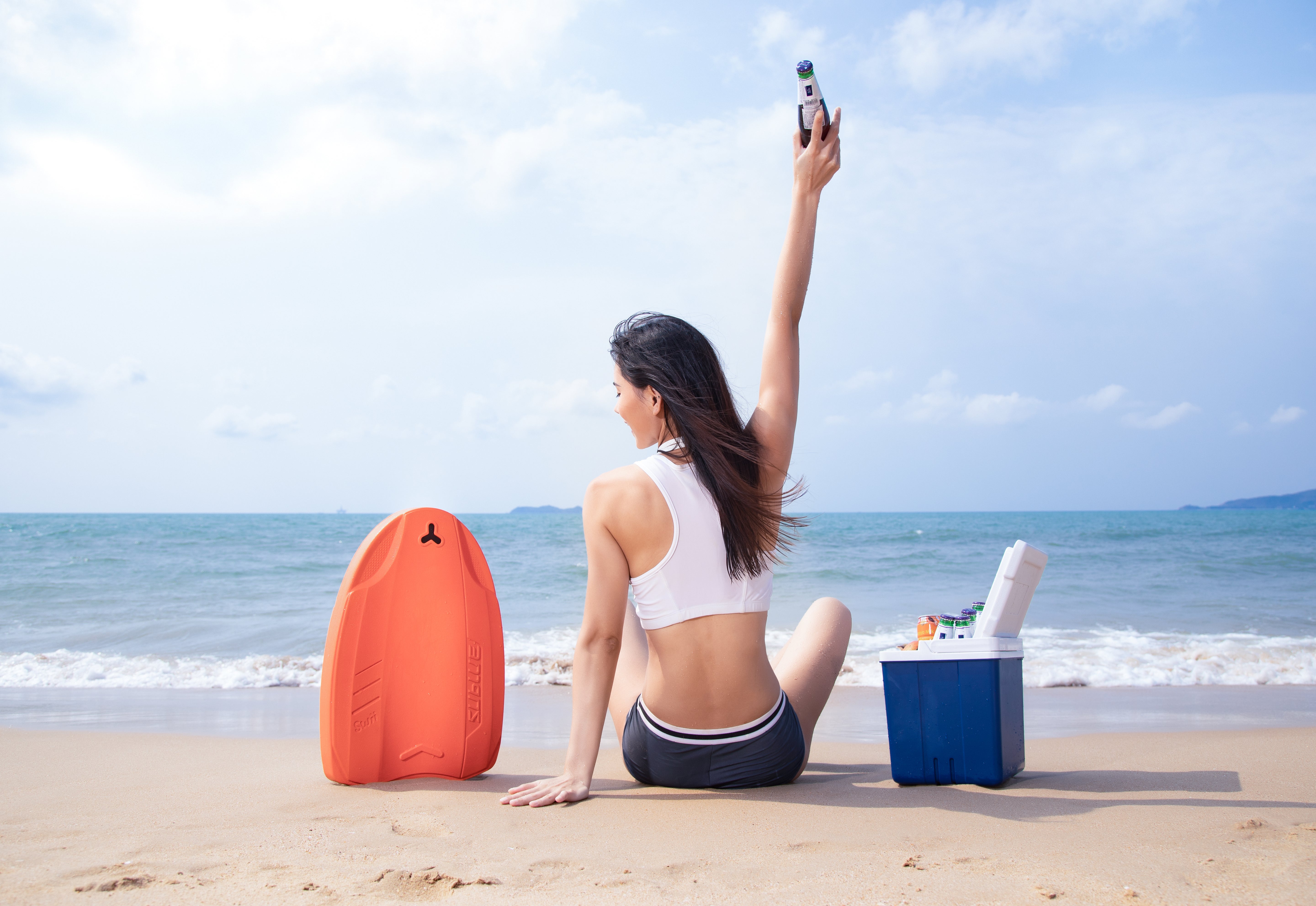 Woman holding SUBLUE Swii kickboard, sitting on the beach by the water.