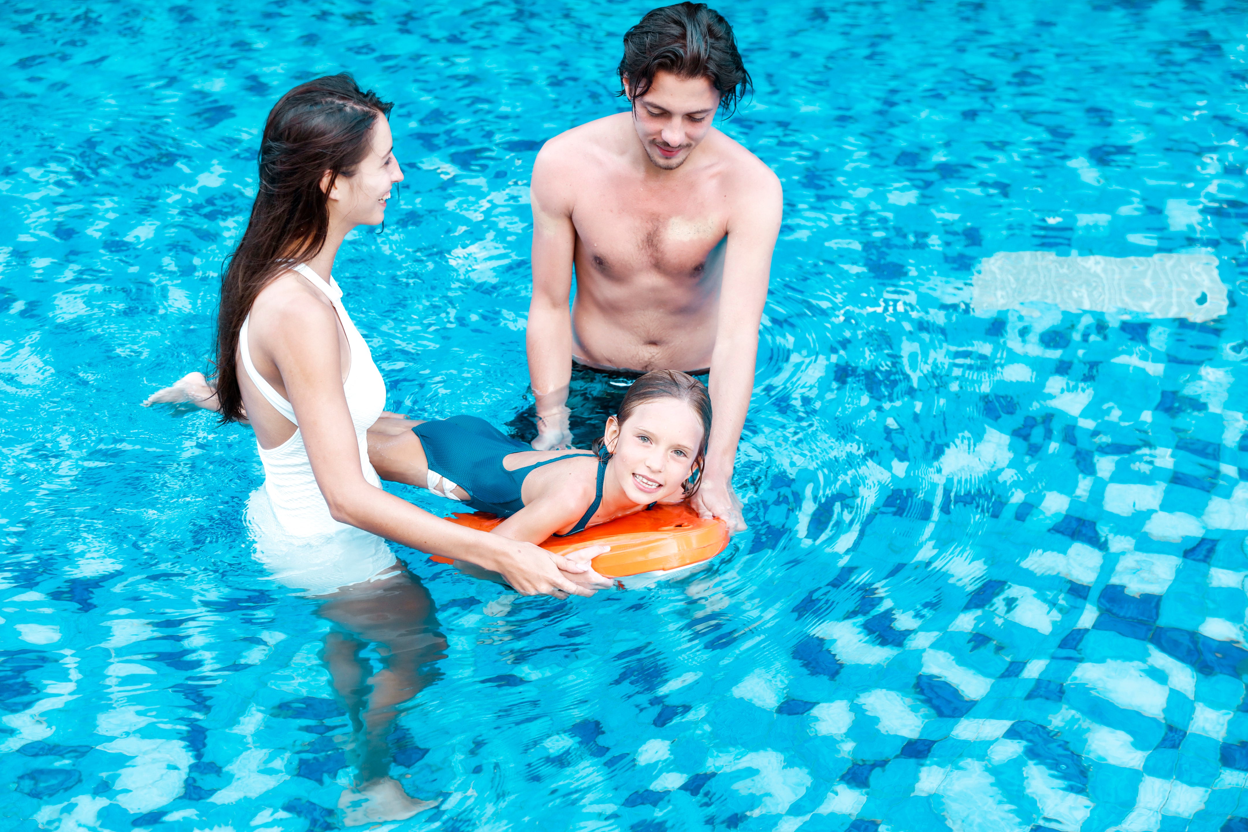 Child supported by adults in a pool, using SUBLUE Swii kickboard for swimming.